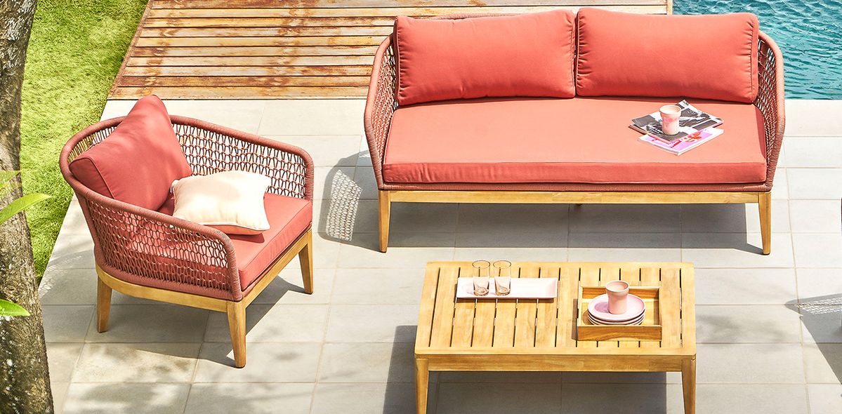 Área externa com sofá e poltronas em tons vibrantes de salmão, dispostos ao ar livre com piscina ao fundo.